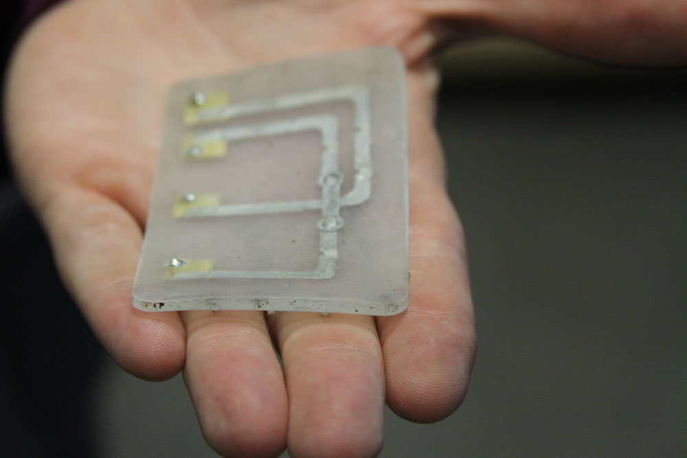 A hand holding out a small piece of physical hardware including a piece of plastic and a metal grid inside.